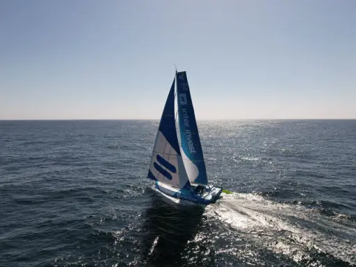 Voilier bleu et blanc "Inter Invest" naviguant sur une mer calme. Matthieu Perraut, skipper, est à la barre.