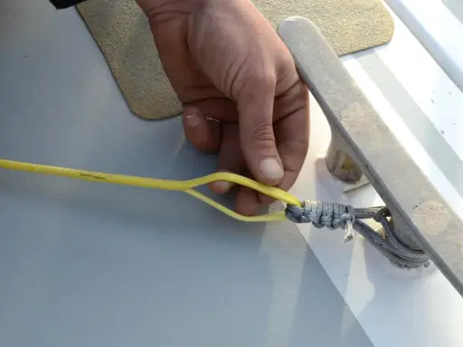 Main d'un marin préparant la ligne de vie d'un voilier, sécurisant une amarre sur un taquet.