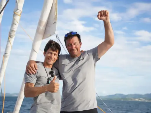 Guillaume Pirouelle et son coéquipier célèbrent une victoire sur l'eau, bras levés et souriants, sous un ciel bleu.