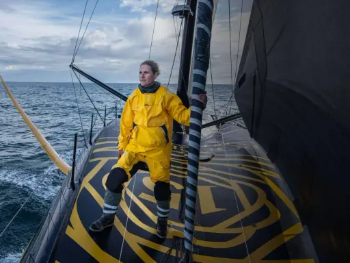 Clarisse Crémer, en tenue de voile jaune vif, se tient fièrement sur le pont d'un voilier, prête à affronter les éléments.