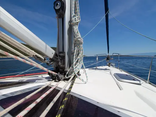 Vue de l'avant d'un voilier naviguant sur une mer bleue. Les cordages sont bien rangés, prêts à hisser le grand mât.