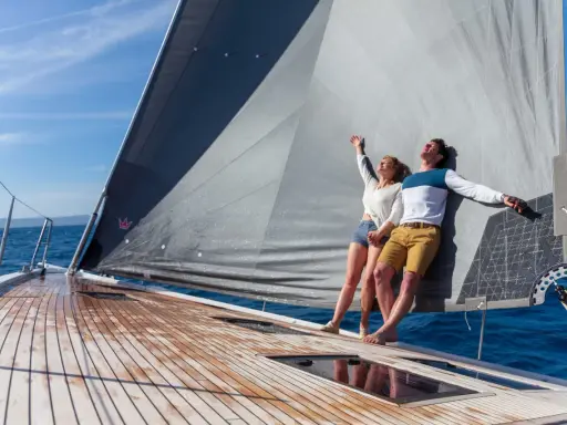 Un couple heureux profite du soleil sur un voilier. Ils semblent avoir fait le bon choix en décidant de choisir un voilier pour leurs vacances.