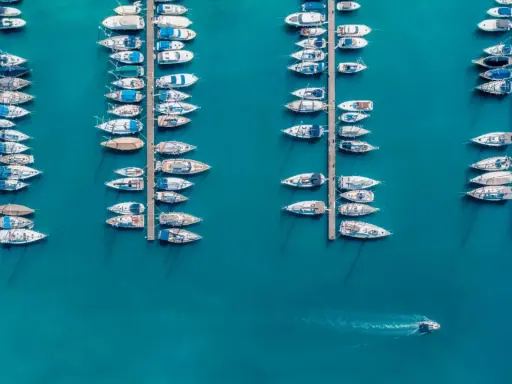 Vue aérienne d'un port où de nombreux voiliers sont amarrés. Un petit bateau navigue, laissant une trace dans l'eau. Le **bloc côtier obligatoire** est bien visible.