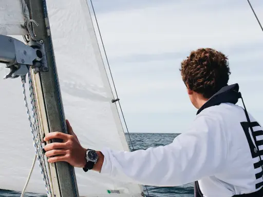 Un jeune homme regarde l'horizon depuis un voilier autonome. La voile blanche est gonflée par le vent.