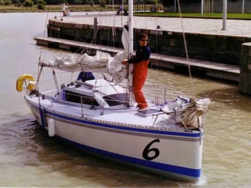 Un homme en salopette rouge prépare un voilier coco, le numéro 6 bien visible sur la proue, prêt à naviguer sur un canal.