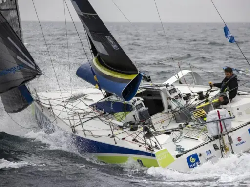 Un skipper navigue sur un voilier blanc et bleu, affrontant les vagues. Le nom "Pierre Quiroga" est visible sur la coque.