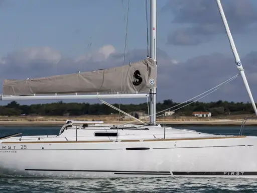 Voilier blanc "First 25 Performance" naviguant sur une mer calme, avec une voile grise arborant un logo noir.