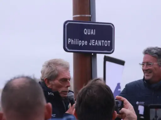Un panneau "Quai Philippe JEANTOT" honore le navigateur. Philippe JEANTOT, entouré, parle au micro.