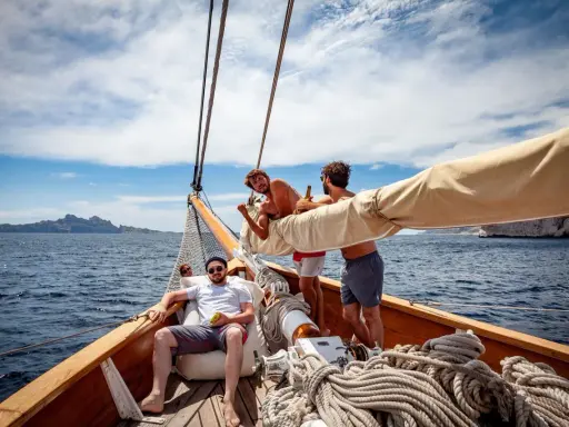 Trois amis profitent du soleil sur un voilier, rêvant d'un tour du monde. L'eau bleue et les falaises en arrière-plan ajoutent à l'aventure.