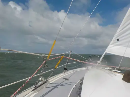 Vue depuis un voilier, mer agitée sous un ciel nuageux. Le gréement et la voile blanche sont visibles. Fiche technique du Challenger Scout.
