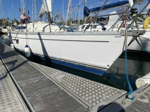Un voilier blanc est amarré à quai. Le soleil se lève, projetant de longues ombres sur le ponton en bois.