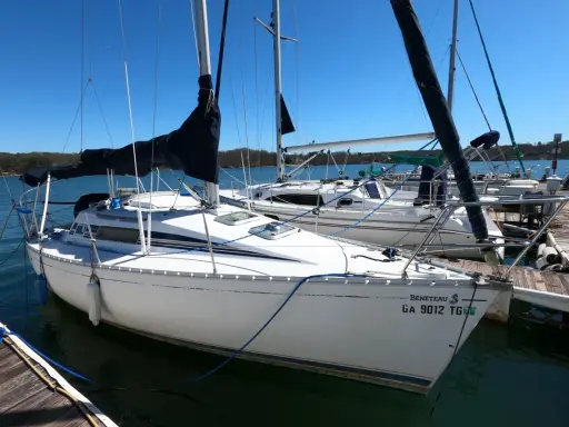 Voilier Beneteau First 235 blanc amarré à un ponton en bois, avec voiles noires et bleues.