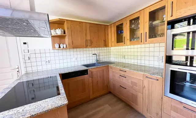 Cuisine en bois clair, avec des placards vitrés rappelant l'intérieur d'un voilier. Le plan de travail en granit et les appareils modernes complètent ce décor chaleureux.
