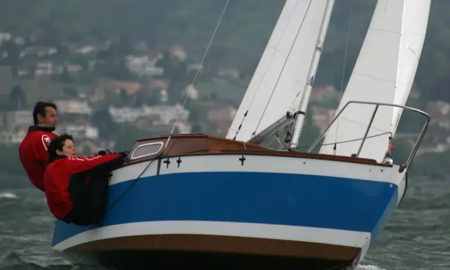 Couple en action sur un voilier transportable hauturier, profitant d'une navigation par temps frais.