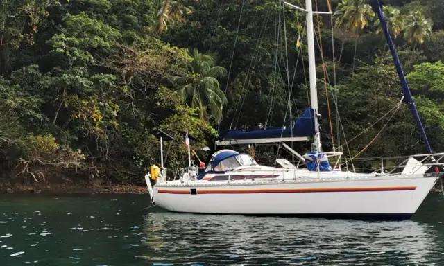 Voilier blanc ancré près d'une côte luxuriante et verdoyante. Le trismus 32 semble prêt pour une aventure tropicale.