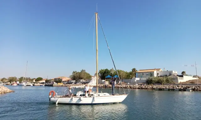 Un voilier atlante navigue sur des eaux calmes, avec des personnes à bord. Le ciel est bleu et dégagé.