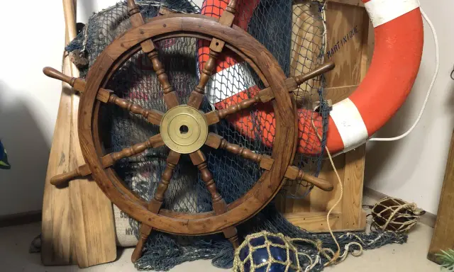 Roue de gouvernail en bois, filet de pêche, bouée de sauvetage orange et pagaies évoquent un safran de bateau prêt pour l'aventure.