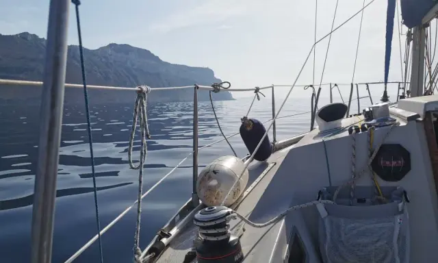Vue depuis un voilier Aquila, naviguant sur une mer calme avec des falaises en arrière-plan. Avis de navigation paisible.
