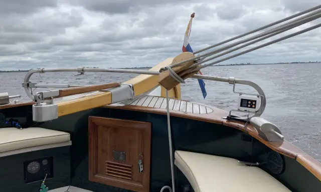 Installation pilote automatique barre franche sur un voilier, avec drapeau néerlandais et ciel couvert.