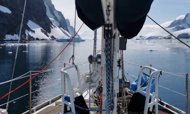 Voile sur un voilier dans un fjord glacé, avec des montagnes enneigées et des icebergs. Le **pen duick 600** navigue paisiblement.