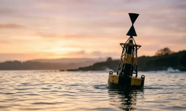 Une bouée jaune et noire, un bms bateau, flotte sur l'eau calme au coucher du soleil.