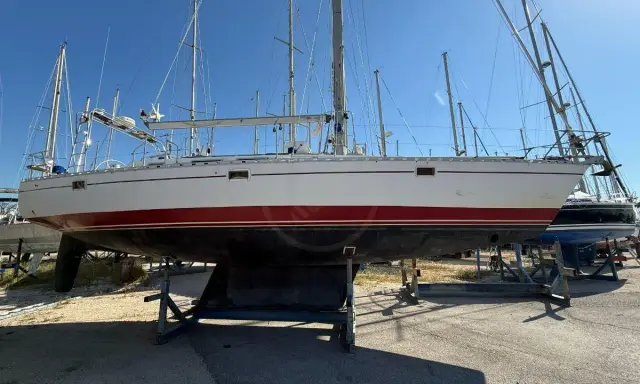 Un voilier blanc et rouge, prêt pour l'aventure, est exposé sur des bers. Ce navire, un modèle de **Gibert Marine**, attend de retrouver les flots.