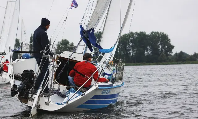 Deux hommes naviguent sur un voilier micro challenger, le vent gonflant les voiles sur un lac calme.