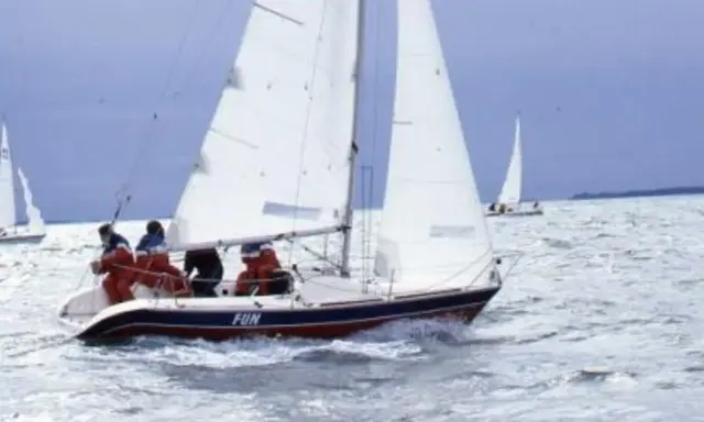 Un voilier nommé "FUN" navigue sur une mer agitée, avec des personnes à bord profitant de la navigation.