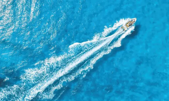 La coque d'un bateau fend les eaux bleues, laissant une traînée blanche de mousse.