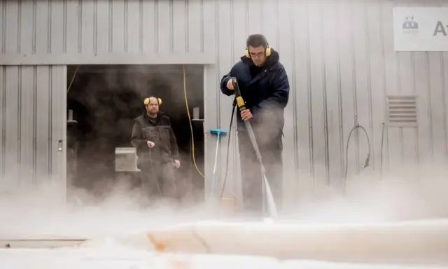 Deux hommes utilisent un nettoyeur haute pression pour nettoyer un voile de bateau avec du savon noir.