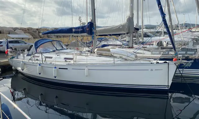 Un voilier Dufour 385 Grand Large blanc, amarré dans un port, reflète son élégance sur l'eau calme.