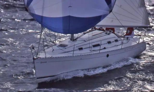 Voilier blanc naviguant sur des eaux agitées, ses voiles bleues et blanches gonflées par le vent. Le nom "DIE-TERRY" est visible sur la coque.
