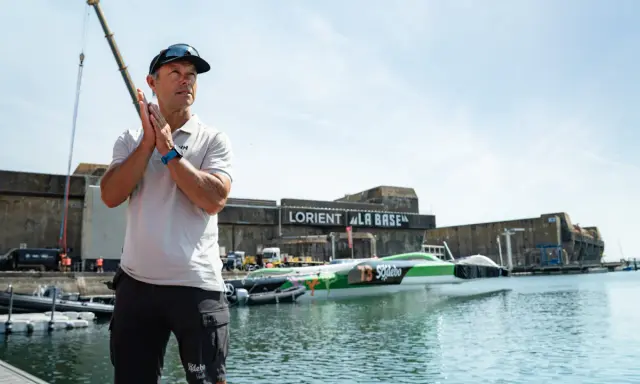 Un homme applaudit devant le trimaran Sodebo Ultim 4, prêt à naviguer.