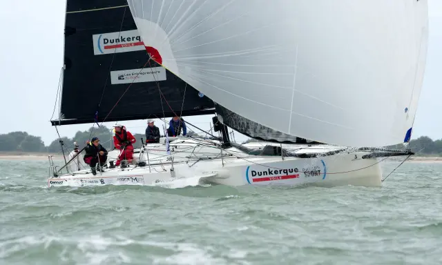 Un voilier "Dunkerque Voile" navigue avec un équipage concentré. Eliott Coville, peut-être à bord, profite de la course.