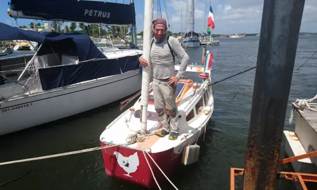 Yann Quenet, prêt pour l'aventure avec son baluchon, pose sur son voilier orné d'une poule.