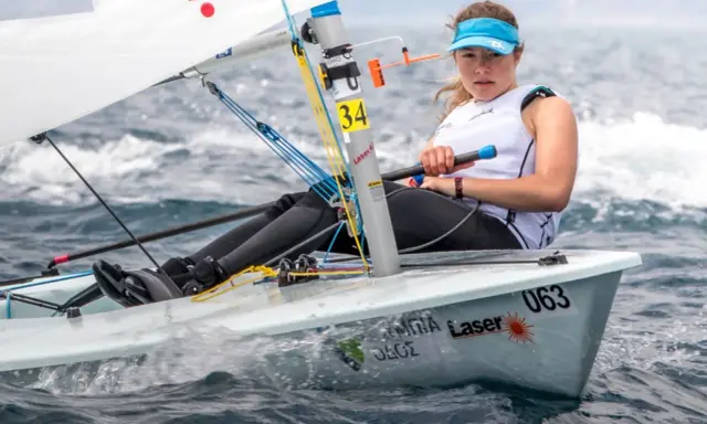 Jeune femme concentrée naviguant en deriveur solo, le bateau #063 fend les vagues.