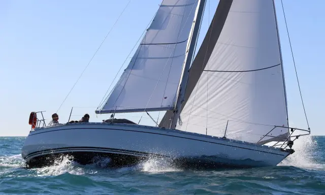 Un voilier Jeanneau Symphony navigue sur une mer agitée, ses voiles blanches gonflées par le vent. Un avis positif pour ce bateau.
