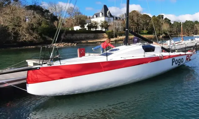 Le voilier Pogo RC, blanc et rouge, est amarré à un ponton. Une personne en blouson rouge est à bord.