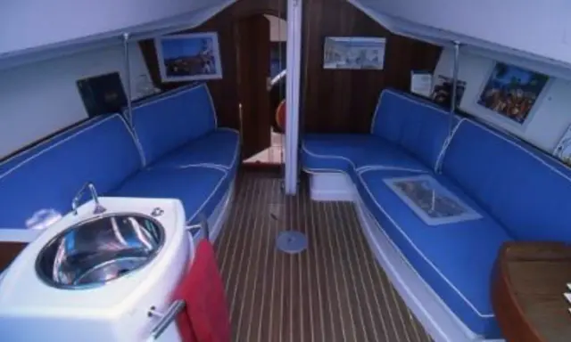 Intérieur du JOD 35, avec banquettes bleues, évier en inox et parquet en bois. Prêt pour une nouvelle aventure en mer.