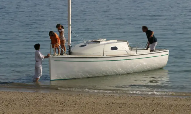 Une famille prépare son voilier, icône 6, pour une sortie en mer. Les enfants montent à bord, impatients de naviguer.