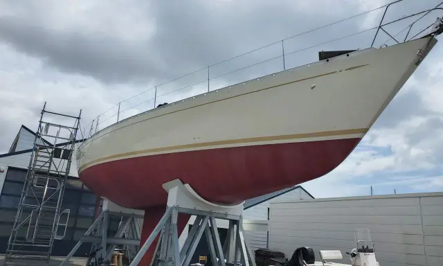 Le nouveau bateau de Jean Le Cam, un voilier blanc et rouge, est sur des supports à côté d'un atelier.