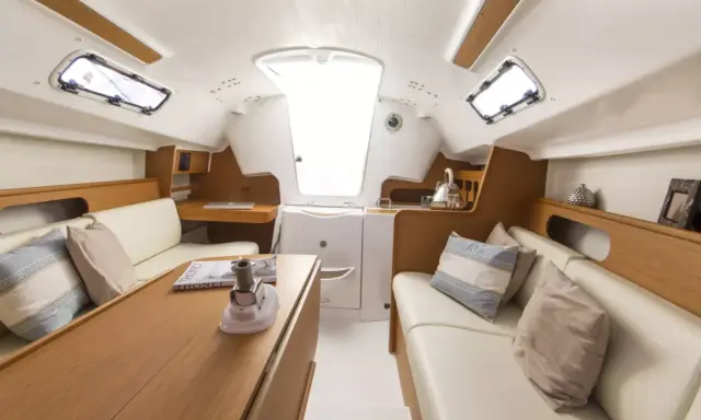 L'intérieur d'un voilier moderne, avec des banquettes en cuir, une table en bois et des hublots. Le premier 25 interieur est lumineux et spacieux.