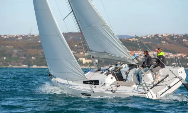Bateau à voile "First 27" en pleine navigation, équipage concentré sur le plan d'eau bleu.