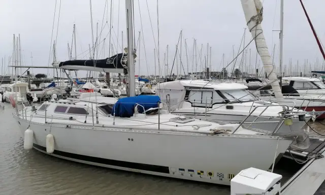 Un voilier blanc, "PEELIN", est amarré dans un chantier naval. D'autres bateaux sont visibles en arrière-plan.
