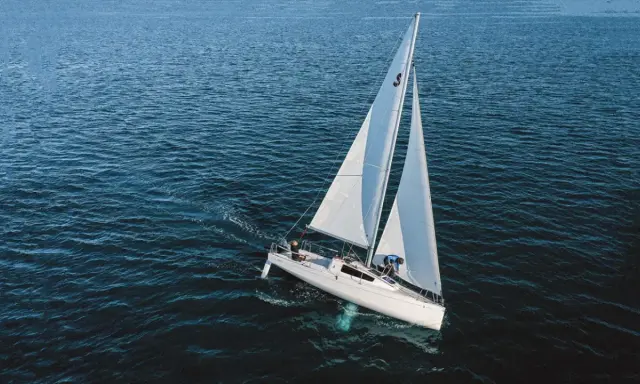 Un voilier blanc navigue sur une mer bleue. Sa quille est visible sous l'eau, stabilisant le bateau.