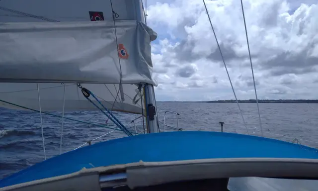 Vue depuis un voilier, avec la liste des voiles d'un bateau gonflées par le vent. La mer est agitée sous un ciel nuageux.
