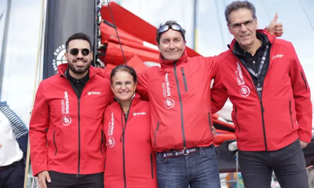 Erwan Thiboumery et trois autres personnes souriantes portent des vestes rouges du Groupe Interaction, devant un bateau.
