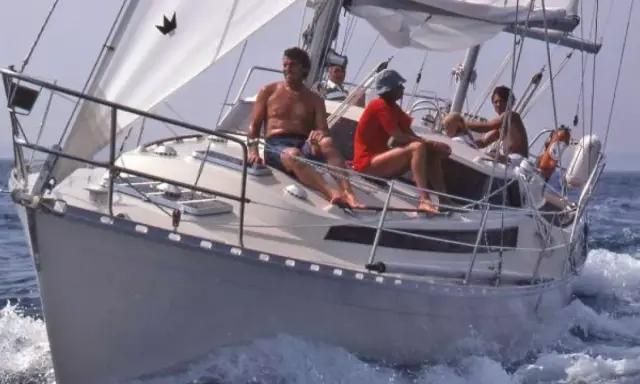 Un groupe profite d'une journée en mer sur ce qui semble être le meilleur voilier fifty, naviguant sur des eaux bleues avec des voiles blanches gonflées par le vent.