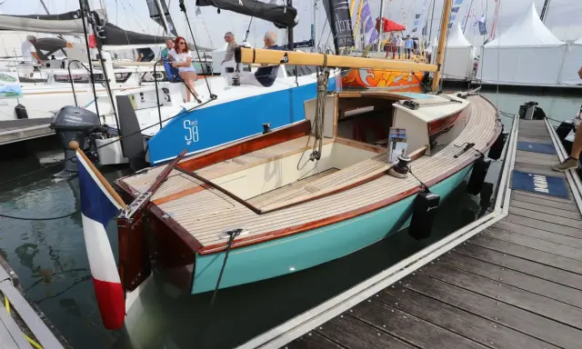 Un élégant belouga bateau, aux finitions bois et coque turquoise, est amarré à quai.