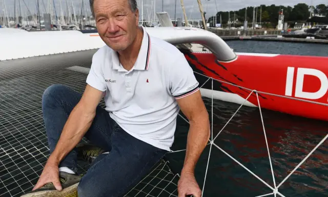 Francis Joyon, marin légendaire, pose sur le filet d'un trimaran rouge vif, prêt pour une nouvelle aventure en mer.